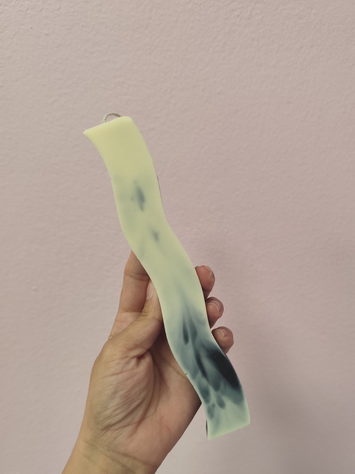 Hand holding a light green object with dark spots against a plain background