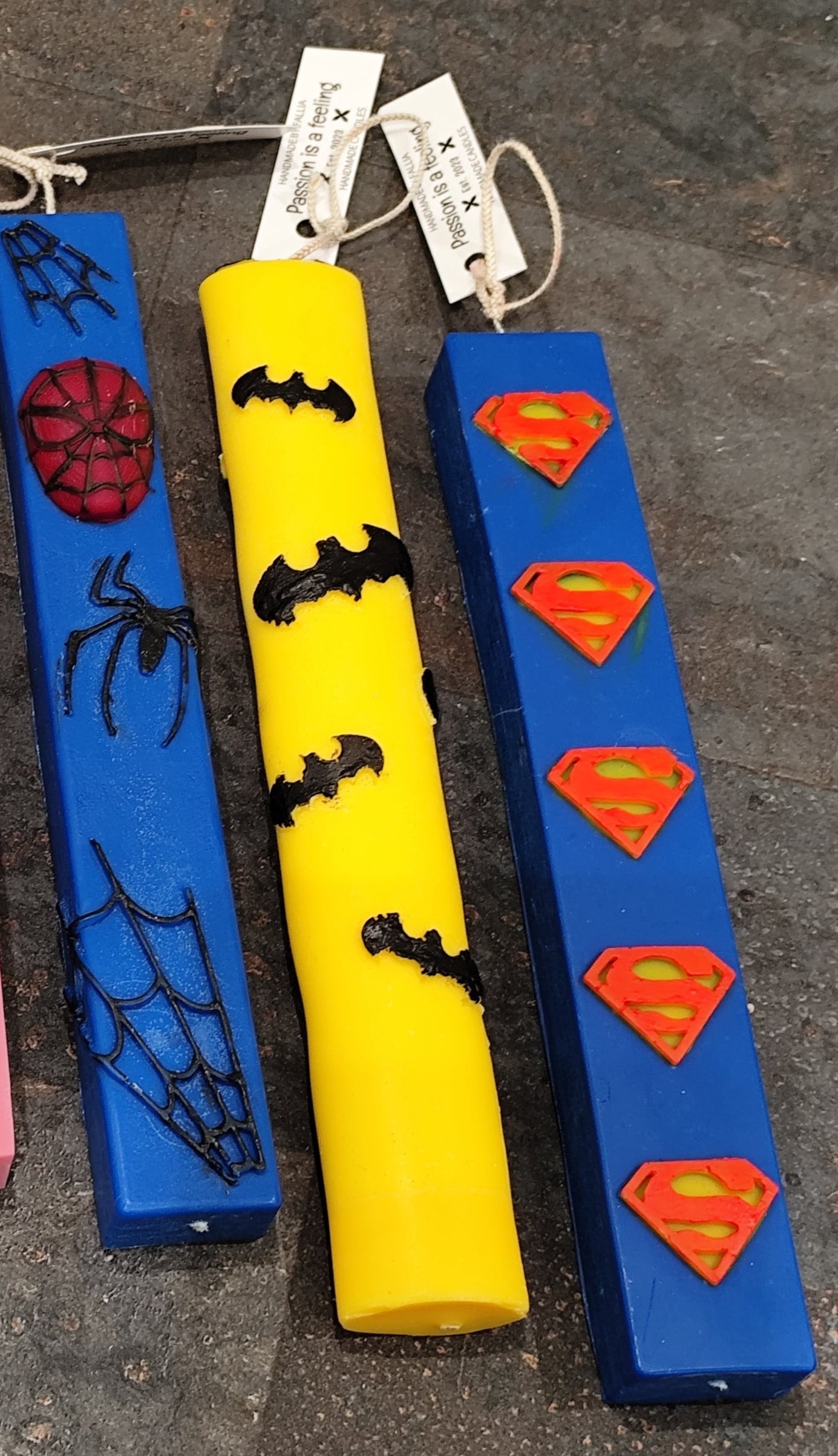 Three colorful Easter candle with superhero logos on a gray surface