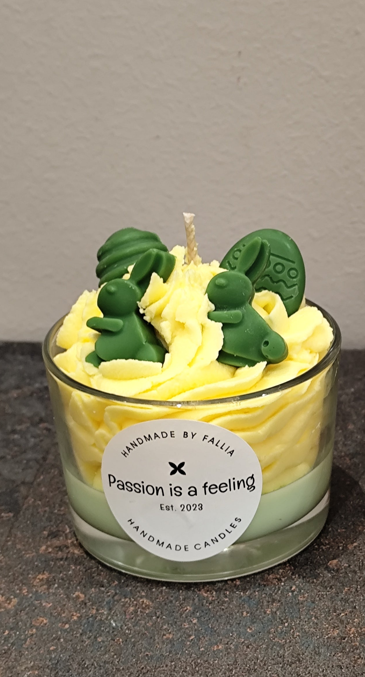Candle with green dinosaur-shaped wicks in a glass container on a dark surface.