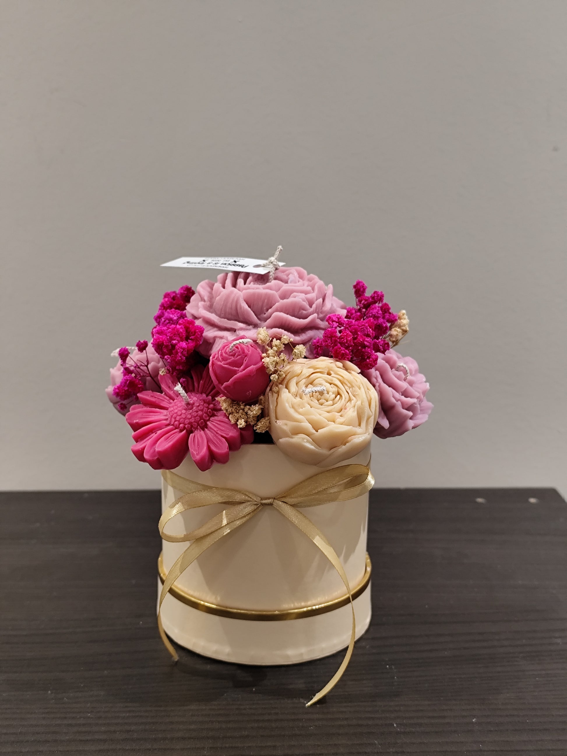 candle flower  in a small white container with gold ribbon on a dark surface.