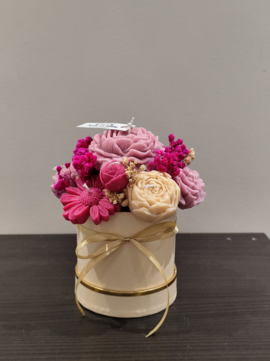 candle flower  in a small white container with gold ribbon on a dark surface.
