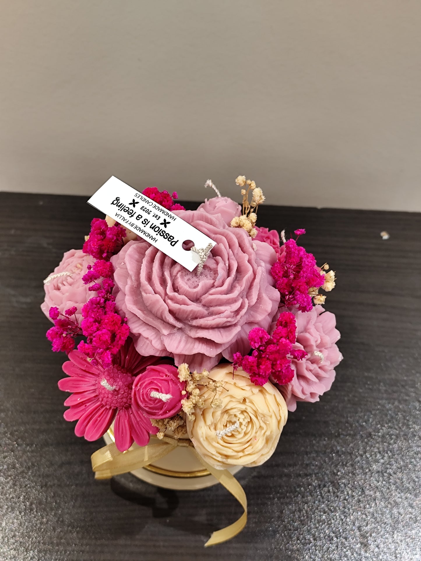 candle flower  in a small white container with gold ribbon on a dark surface.