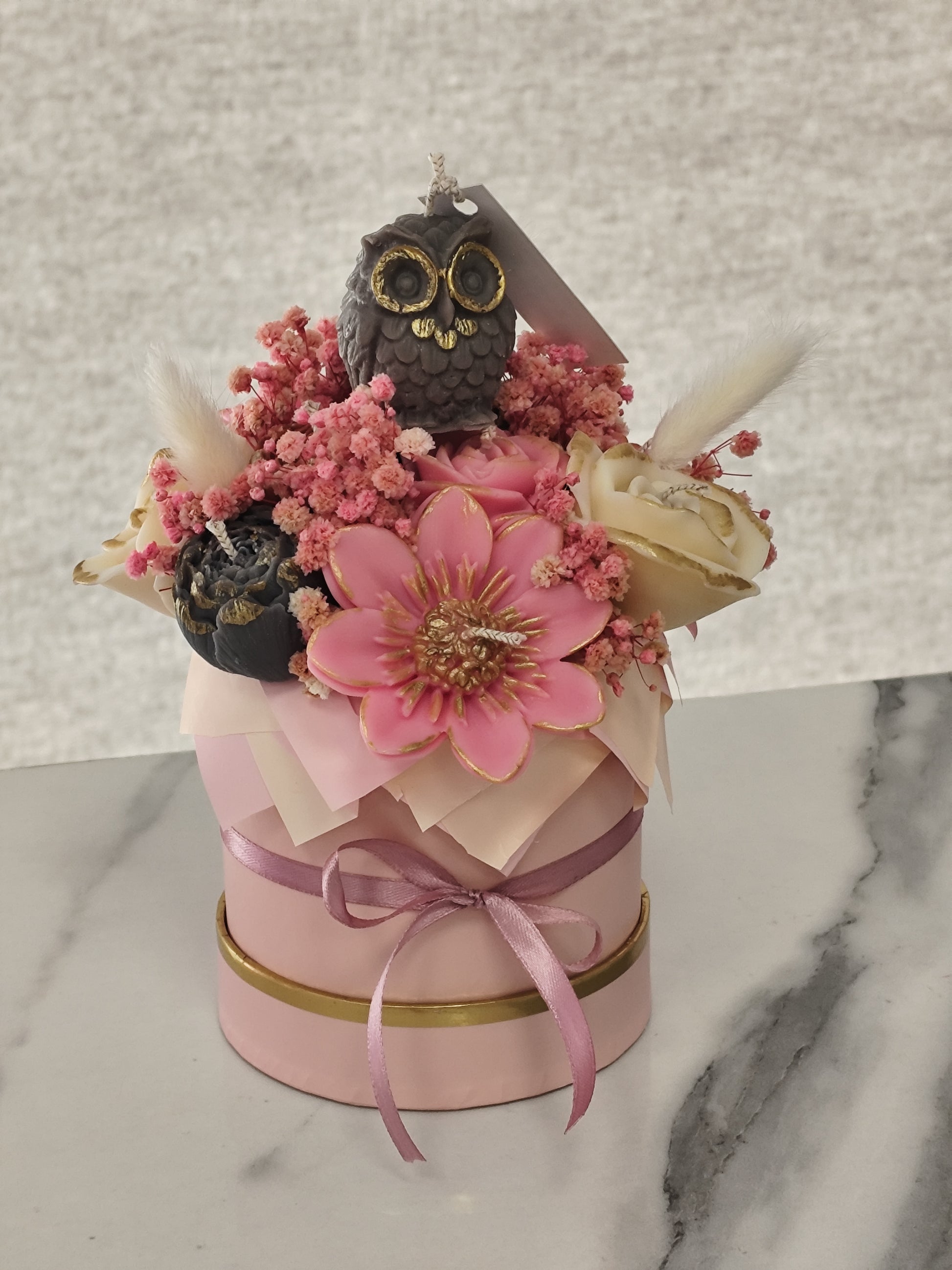Candleflowers and owl figurine in a pink box on a marble surface.