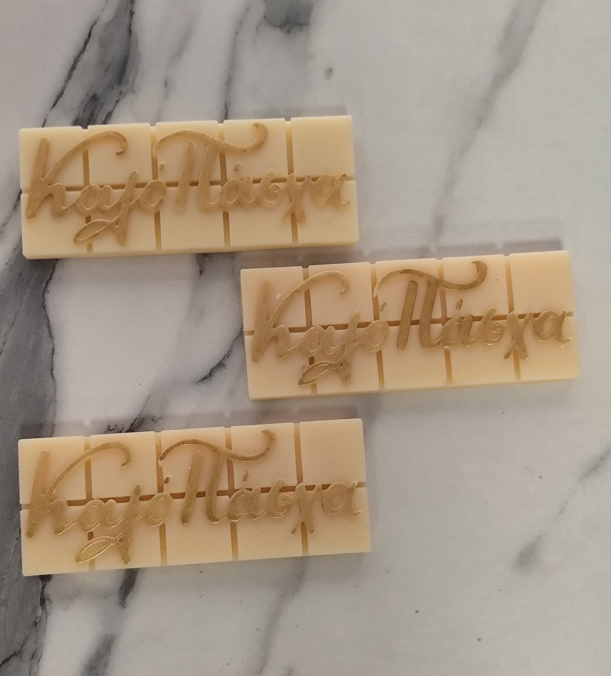 Three rectangular wax bars with engraved text on a marble surface