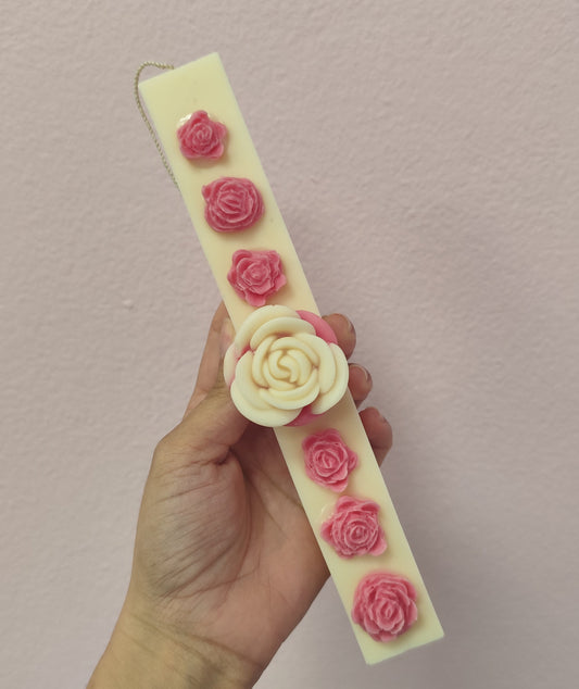 Hand holding a bar of soap with pink and white rose designs against a plain background
